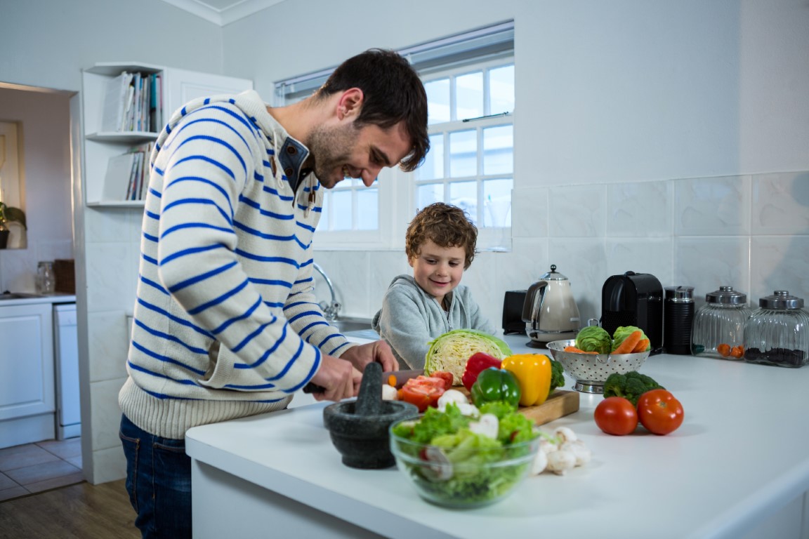 Boy looking while father chopping vegetables in the kitchen